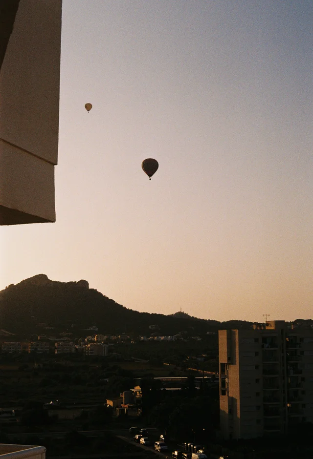 Hot-air balloons above a hillside town at sunset