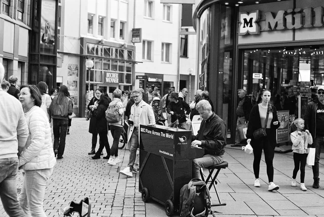 A pianist playing on a busy cobbled shopping street in black and white