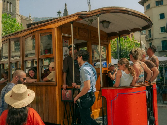 Passengers boarding a red and wooden tram on a sunny city street